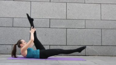 Genç kadın yoga yaparken spor ve kentsel arka plan ve pembe yoga mat pilates fitness egzersizleri üzerinde gri