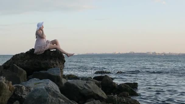 Sommermode Hipster Frau in schönem Kleid sitzt auf dem Stein am Strand — Stockvideo