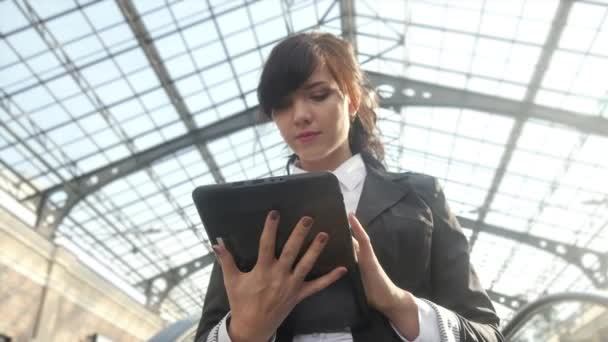 Attractive businesswoman using a digital tablet while standing on escalator in an office building. — Stock Video