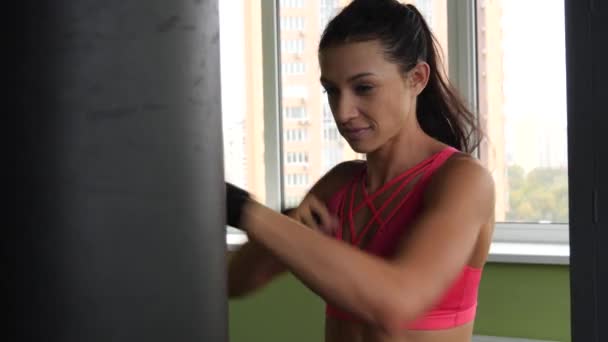 Atraente kickboxing misto raça mulher formação saco de perfuração no estúdio de fitness força feroz em câmera lenta . — Vídeo de Stock