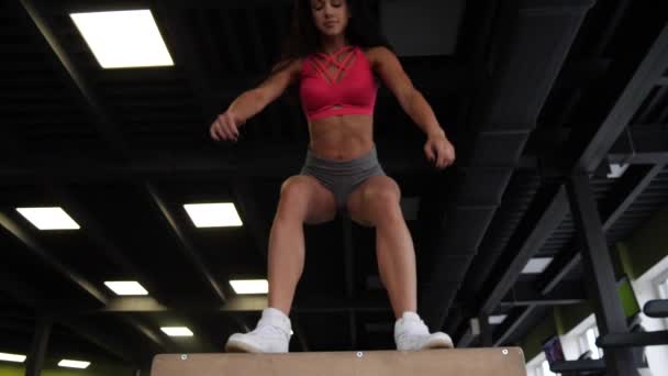 Латиноамериканка прыгает на деревянную коробку в тренажерном зале для кроссфитов — стоковое видео