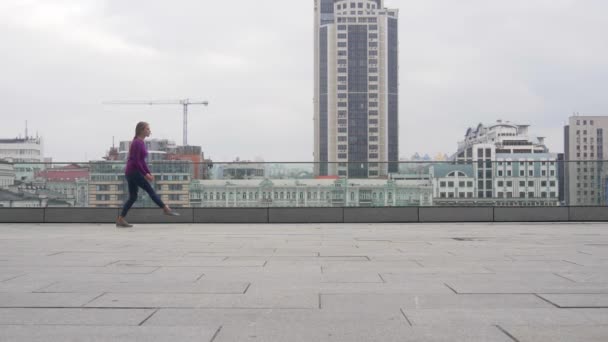 Молодая привлекательная женщина занимается акробатикой на фоне городского пейзажа — стоковое видео