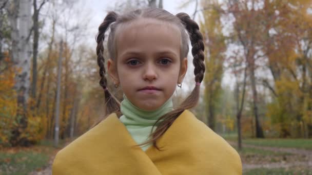 카메라에 웃는 어린 아이 여자 아이의 초상화를 닫습니다. 소녀는 공원에서 노란 코트를 입으십시오 — 비디오