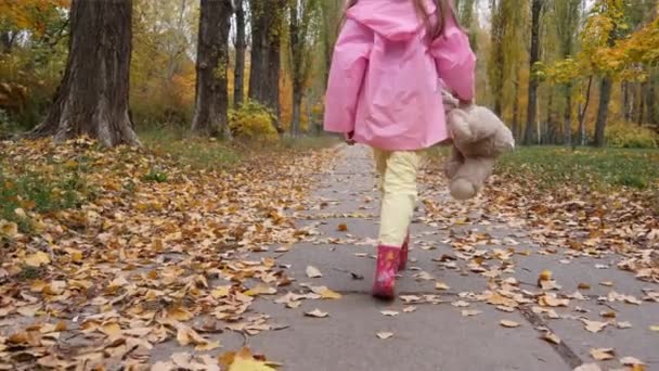 Fröhliches kleines blondes Mädchen spielt mit Teddybär im Herbstpark — Stockvideo