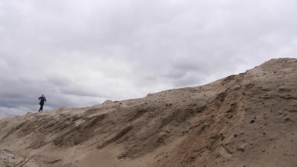 Concentrated woman jogger with a slender figure is engaged in run at desert. Dark storm clouds sky at background. — Stock Video