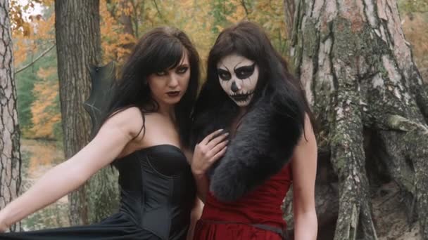 Young halloween girl friends in black and red witch dress having fun in the forest park with traditional autumn holiday symbol of orange spooky pumpkin outdoor — Stock Video