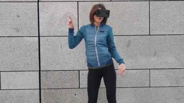 Jonge vrouw die van een vr bril, hoofdtelefoon, gelukkig virtuele spelen en het kijken naar video's buitenshuis in de stad straat dansen. Emoties — Stockvideo