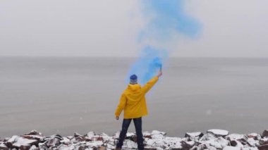 Mavi duman duman donmuş deniz önünde sarı montlu adam görünümünü arka. Ön planda düşen kar
