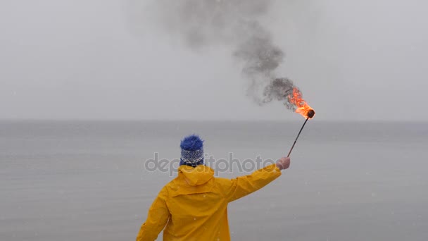 凍った海の背景に黄色のコートにたいまつを持った男の後姿。フォア グラウンドに雪が降りました — ストック動画