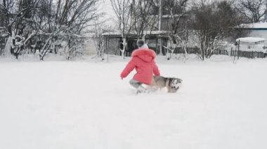 Genç kız açık havada ağır çekimde karda Siberian dış yapraklar malamute köpekle oynamayı