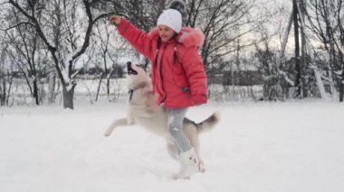 Genç kız açık havada ağır çekimde karda Siberian dış yapraklar malamute köpekle oynamayı