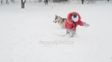 Genç kız açık havada ağır çekimde karda Siberian dış yapraklar malamute köpekle oynamayı