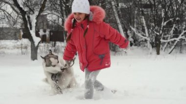 Genç kız açık havada ağır çekimde karda Siberian dış yapraklar malamute köpekle oynamayı