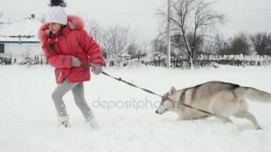 Genç kız açık havada ağır çekimde karda Siberian dış yapraklar malamute köpekle oynamayı