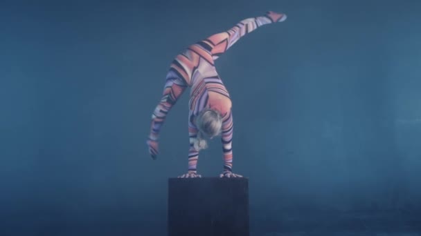 Unga flexibla blond cirkus akrobat poserar i studio i kostym. Gör equilibre balans handstående på en kub. — Stockvideo