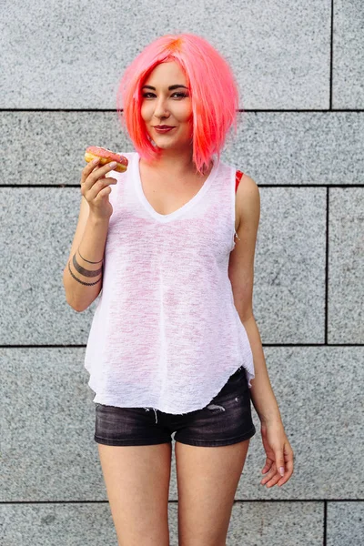 Beauty fashion mixed race model with pink wig girl taking colorful donut. Funny joyful woman with sweets, dessert. Diet, dieting concept. Junk food, Slimming, weight loss