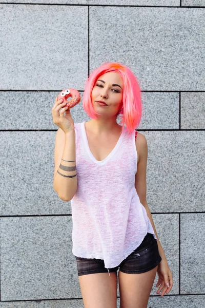Beauty fashion mixed race model with pink wig girl taking colorful donut. Funny joyful woman with sweets, dessert. Diet, dieting concept. Junk food, Slimming, weight loss