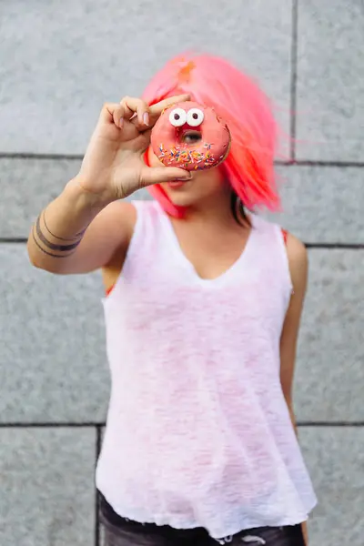 Güzellik moda karışık ırk modeli ile renkli donut alarak pembe peruk kız. Komik neşeli kadın tatlılar, tatlı. Diyet, diyet kavramı. Abur cubur, zayıflama, kilo kaybı