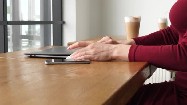 Geschäftsfrau im roten Kleid arbeitet im Café am Laptop und trinkt Latte Coffee — Stockvideo