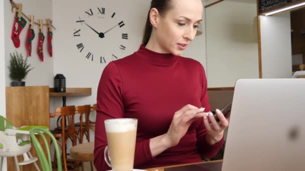 Frau mit Smartphone im Café trinkt Kaffee lächelnd und telefoniert mit Handy. schöne lässige weibliche Profi in rotem Kleid auf dem Handy. Kaukasisches Modell. — Stockvideo