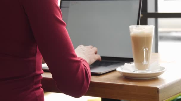 Бізнес жінка в червоний плаття працюють на портативний комп'ютер в кафе латте пити каву — стокове відео