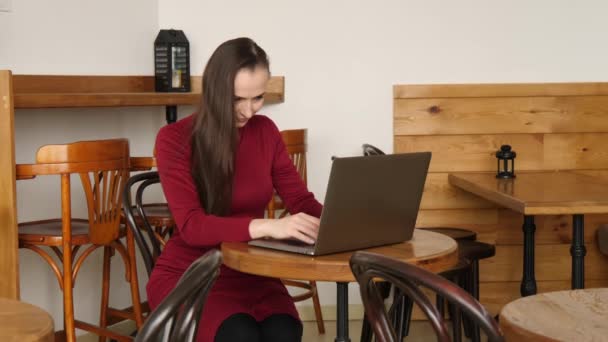 Mulher de negócios em vestido vermelho que trabalha no computador portátil no café que bebe café latte — Vídeo de Stock