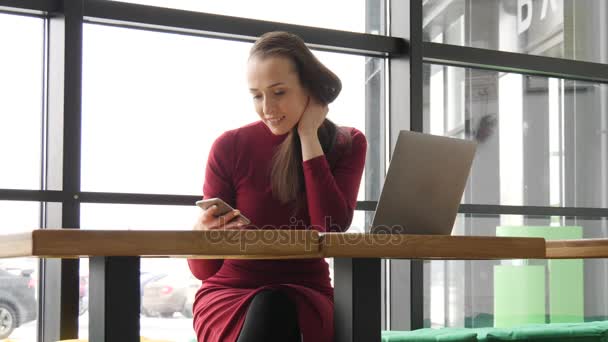 Femme utilisant l'application sur smartphone dans le café en buvant du café souriant et textos sur téléphone mobile. Belle professionnelle décontractée en robe rouge avec téléphone portable — Video