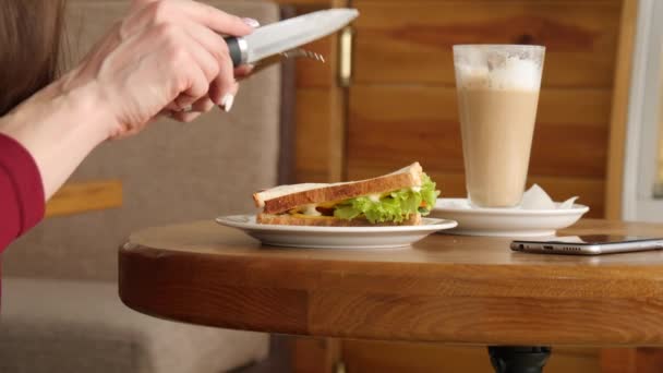 Kırmızı elbiseli kadın ona sandviç yiyecek city Café dilim kesmek. Smartphone bir tablo — Stok video