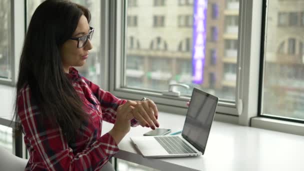 Hipster mulher de raça mista usando smartwatch e trabalhando no laptop pc no café — Vídeo de Stock