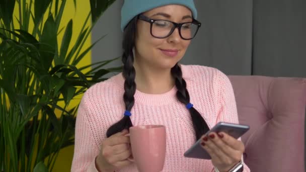 Mujer hipster de raza mixta sentada en la cafetería, tomando café y usando un teléfono inteligente — Vídeo de stock