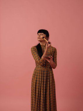 Karışık ırk kadın makyaj gül pembe bir arka plan üzerinde fırça ile uygulanması