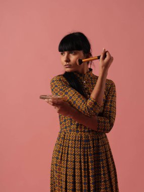 Karışık ırk kadın makyaj gül pembe bir arka plan üzerinde fırça ile uygulanması