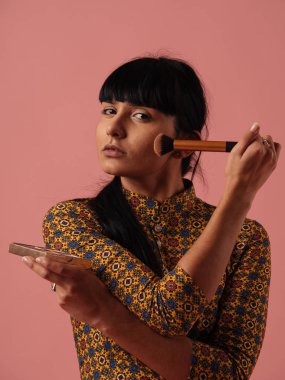 Karışık ırk kadın makyaj gül pembe bir arka plan üzerinde fırça ile uygulanması