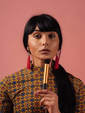 Karışık ırk kadın makyaj gül pembe bir arka plan üzerinde fırça ile uygulanması