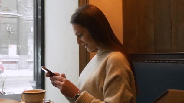 Mujer bonita usando la aplicación en el teléfono inteligente en la cafetería beber café — Vídeo de stock