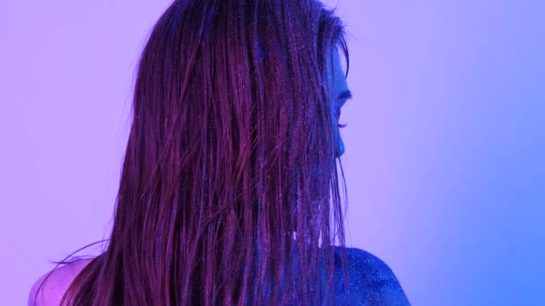 Mooie vrouw met Sparkles op haar gezicht in ultraviolet licht — Stockvideo