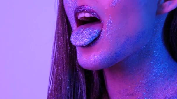 Mooie vrouw met Sparkles op haar gezicht en de tong in ultraviolet licht — Stockvideo