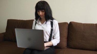 Dizüstü evde kullanan genç kadın kanepede oturan