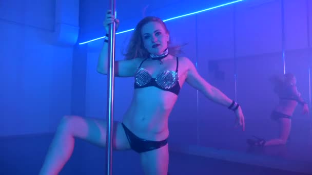 Молодая сексуальная стройная женщина танцует с пилоном в темном интерьере — стоковое видео