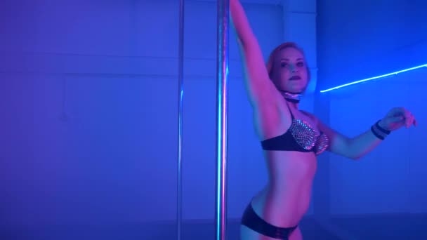 Молодая сексуальная стройная женщина танцует с пилоном в темном интерьере — стоковое видео