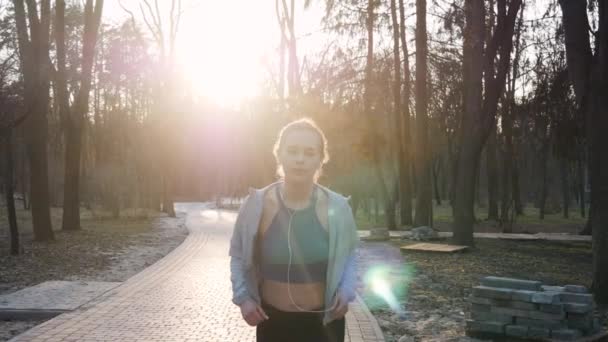 Sportieve vrouw buitenshuis in slowmotion op concrete spoor in park luisteren naar muziek uitgevoerd. Gezonde fitness concept — Stockvideo