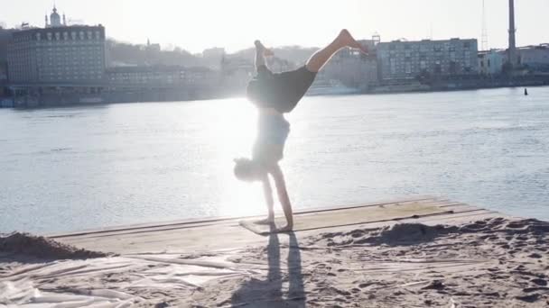 年轻的白种人放松练习瑜伽健身运动在附近的平静河与城市背景的海滩 — 图库视频影像