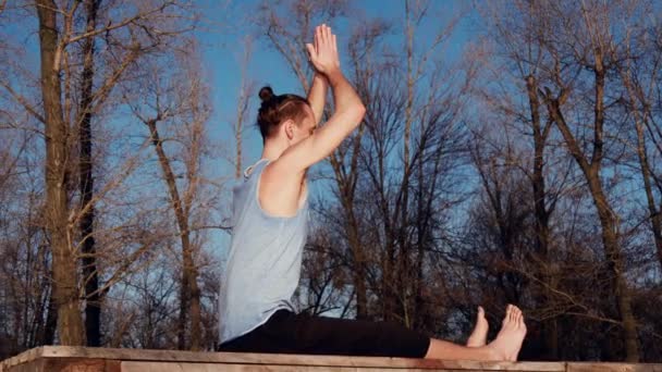 Kaukasiska ung avkopplande genom att praktisera yoga fitness motion på stranden nära lugn flod med staden på bakgrunden — Stockvideo