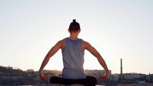 Junger kaukasischer Mann entspannt sich durch Yoga-Fitness-Übungen am Strand in der Nähe des ruhigen Flusses mit Stadt im Hintergrund — Stockvideo