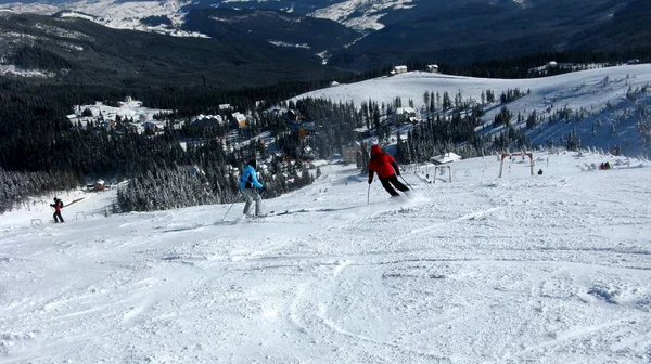 Flera skidåkare gå ner snöiga backarna i skidorten, v — Stockfoto