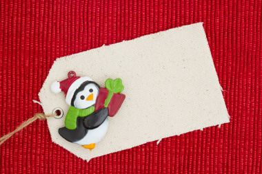A cloth gift tag with a Christmas penguin on shiny red material clipart