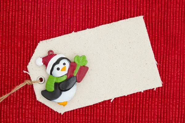 Une étiquette cadeau en tissu avec un pingouin de Noël sur un matériau rouge brillant — Photo