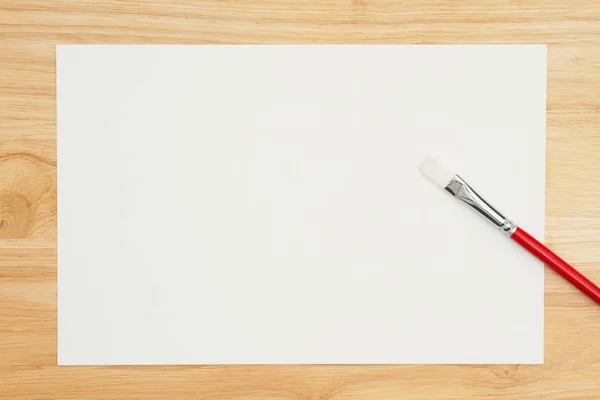 A red paint brush with watercolor paper on wood desk — Stock Photo, Image