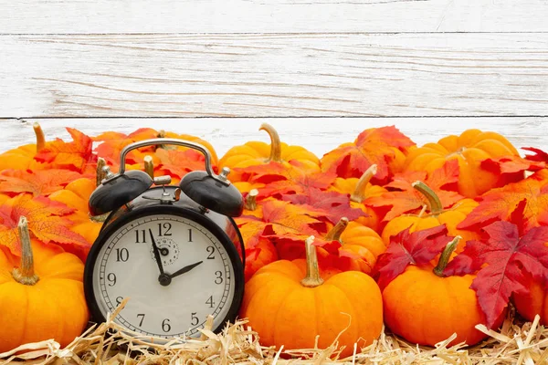 Reloj despertador retro con calabazas naranjas con hojas de otoño sobre paja — Foto de Stock