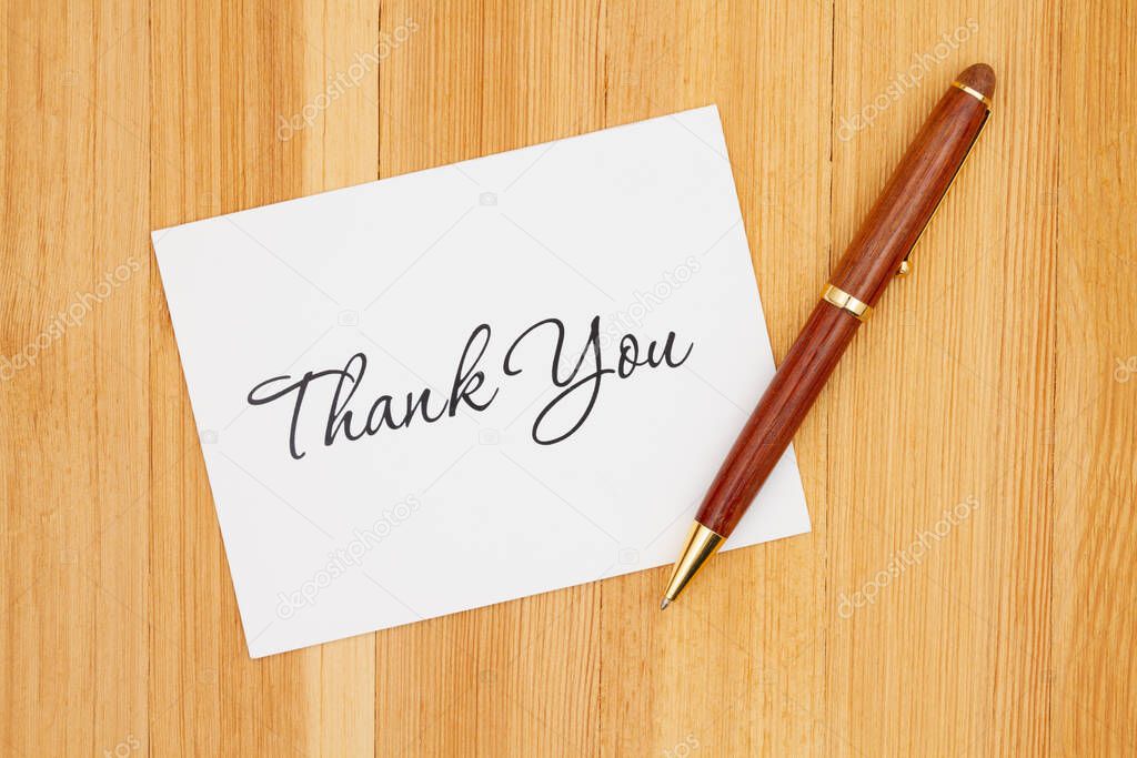 White Thank You greeting card with pen on a pine wood desk